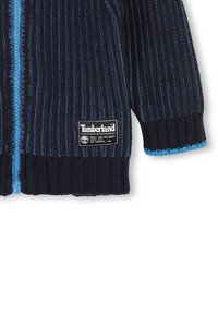 Maglione zippato a coste blu navy con zip blu a contrasto, patch con logo in basso a sinistra e polsini testurizzati.