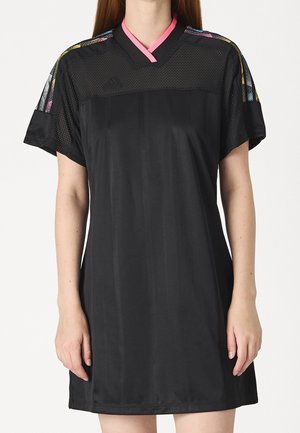 Femme portant une robe noire à manches courtes avec des épaules en maille, des rayures multicolores sur les manches et un détail de col rose.