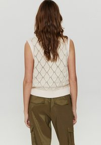 Krämfärgad ärmlös stickad tröja med en diamantmönster, ribbat avslut och avslappnad passform. Matchad med olivgröna cargobyxor.