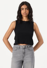 Fekete, cropped tank top ribbed textúrával, hullámos nyakkivágással és egy kis fekete masnival a közepén. Szürke, magas derekú farmerral viselve.