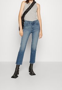 Světle šedý bezramenný top v kombinaci se středně modrými džíny s roztrhaným lemem a černými koženými botami na podpatku se čtveratou špičkou.