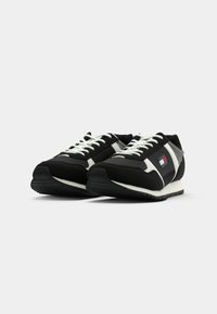 Black athletic sneakers with white laces and accents, featuring mesh panels and a multi-colored logo patch on the side. Rubber sole.