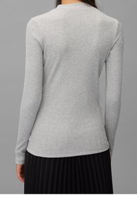Graues gestreiftes Langarmshirt mit rundem Halsausschnitt. Das Material wirkt weich und hat einen figurnahen Schnitt. Der Saum ist am unteren Ende leicht gewellt.