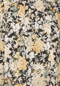 Blommig tyg med stora gula och vita blommor på en svart bakgrund, med gröna blad och en texturerad yta. Veck synliga.