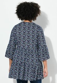 Blusa floreale con maniche a campana, sfondo blu navy, caratterizzata da motivi floreali bianchi, azzurri e viola. Corpo aderente con orlo svasato.