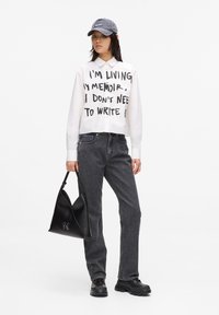 Hvit forkortet skjorte med svart tekst, grå denimjeans, svart strukturert håndveske og grå caps. Svarte sko med tykke såler.