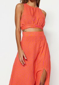 Ensemble crop top et jupe rayés rose et orange, avec une coupe ajustée, un détail ajouré et un motif géométrique. Texture de tissu lisse.