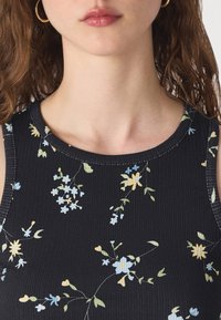 Top a canotta nero a costine con motivo floreale di fiori blu e gialli su gambi verdi, scollatura rotonda e design senza maniche.