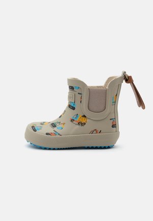 Botte de pluie beige pour enfants avec des imprimés colorés de véhicules de construction, panneau latéral élastique, semelle bleue et languette marron à l’arrière.
