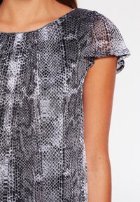 Top a maniche corte con motivo a stampa di serpente in nero e grigio, realizzato in tessuto leggero, con scollatura rotonda e morbide maniche arricciate.