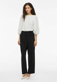 Lys grå tekstureret bluse med brede ærmer, parret med sorte højtaljede bukser og nude spidse hæle. Enkel, elegant design.