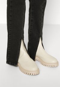White rubber boots with ridged soles, paired with black denim jeans featuring side slits, creating a contrast in color and texture.