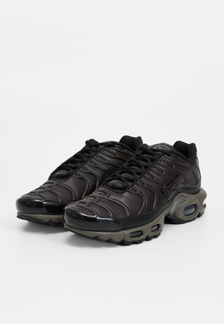 Zapatillas deportivas negras con una parte superior texturizada, punta redondeada y amortiguación de aire visible. Presenta un acento negro brillante en la suela.