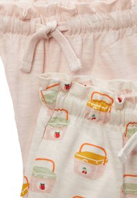 Shorts en coton rose clair avec une taille élastique et un détail en nœud ; shorts crème présentant un motif de fruits et de panier de pique-nique.