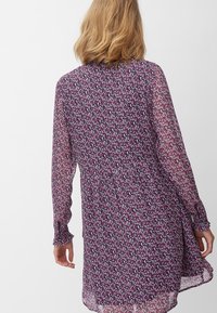 Lila blommig klänning med långa, genomskinliga ärmar och en draperad midja. Har ett fint mönster med små rosa och vita blommor.