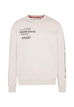 Helle beigefarbene Sweatshirt mit Rundhalsausschnitt, langen Ärmeln und gerippten Bündchen. Mit bedrucktem Text in Schwarz und Orange, sowie Branding auf der Vorderseite und den Ärmeln.