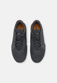 Grå träningsskor med en nätövre, texturerade detaljer och en kontrasterande orange innersula. Har snörning och en diskret logotyp.