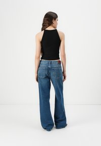 Black ribbed tank top with a high neckline paired with blue wide-leg jeans featuring back pockets and a leather patch on the waistband.