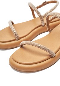 Tan flat sandals with two narrow straps embellished with rhinestones. Soft cushioned sole and a sleek design. Lightweight material.