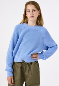 Lichtblauwe gebreide trui met ribbeltextuur, ronde halslijn en lange mouwen, gecombineerd met olijfgroene broek met een trekkoord in de taille.