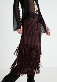 Top negru din material transparent cu margini franjurate, asortat cu o fustă plisată bordeaux care are detalii cu franjuri la tiv. Țesătură texturată, design stratificat.