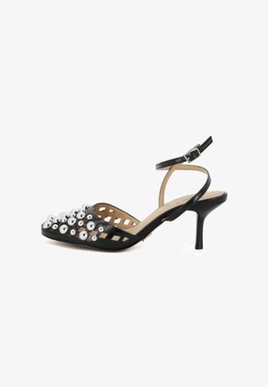 Décolleté slingback in pelle nera con punta appuntita, borchie sferiche argentate e lati traforati, dotata di cinturino alla caviglia con fibbia.