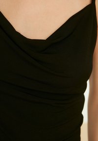 Haut noir sans manches avec un col drapé et des détails en tissu froncé, présentant une texture lisse et un drapé subtil.