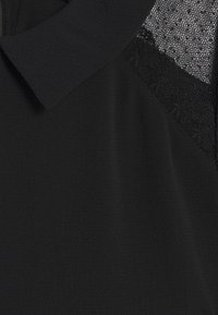 Zwarte top met een kraag, voorzien van getextureerd mesh en kanten accenten aan één zijde. Zachte, gladde stof met een subtiele glans.