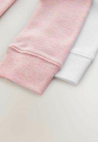 Rosa och vita bomullstygmanschetter med ribbat mönster. Den rosa manschetten har ett subtilt prickigt mönster; den vita manschetten är slät.