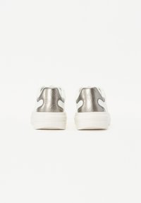 Weiße Sneaker mit einer strukturierten, metallisch silbernen Fersenkappe, die dekorative Muster und ein robustes Sohlen-Design aufweisen.