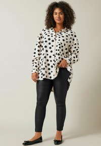 Roomde bloem blouse in crème en zwart, lange mouwen, knopen aan de voorkant, gebogen zoom. Gecombineerd met glanzende zwarte leggings en zwarte ballerina's.