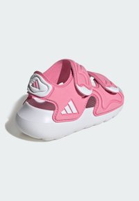 Różowy sportowy sandał z teksturowaną gumową podeszwą, regulowanymi paskami na rzep oraz białymi akcentami, prezentujący sportowy design i otwarte boki.