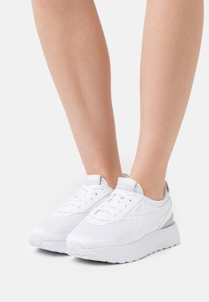 Chaussures de sport blanches avec une tige en mesh texturé, un bout arrondi, des lacets plats et une semelle épaisse avec un subtil accent gris au talon.