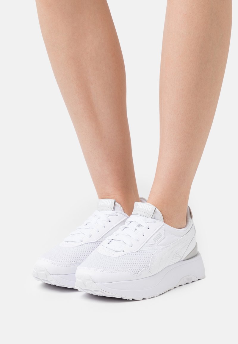 Chaussures de sport blanches avec une tige en mesh texturé, un bout arrondi, des lacets plats et une semelle épaisse avec un subtil accent gris au talon.