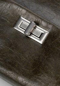 Tessuto verde scuro e texturizzato, con un metodo di chiusura metallico rettangolare. La superficie presenta un motivo sgualcito, che aggiunge interesse visivo.