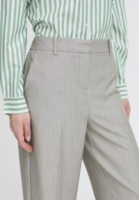 Pantalones a medida de color gris claro hechos de tela suave, con frente plano, bolsillos laterales y una cintura estructurada.