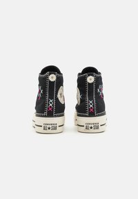 Zapatillas altas de lona negras con detalles bordados en azul y rosa. Presentan un contraste de costura blanca y una suela de goma clásica.