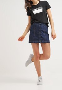 Svart t-shirt med grafiken "SAN FRANCISCO", i kombination med en mörkblå denim A-linje kjol med framknappar och vita sneakers.