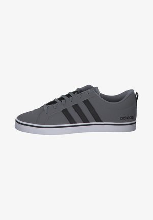 Zapatilla gris con tres rayas negras, parte superior de sintético liso, cordones en la parte frontal, entresuela blanca y marcaje negro en el talón.