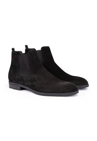 Par de botas Chelsea negras de ante con paneles laterales elásticos y tacones bajos, mostradas sobre un fondo blanco.
