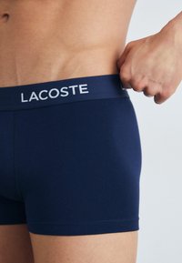 Marineblaue Boxershorts mit elastischem Bund; verfügt über das weiße "LACOSTE"-Logo. Glatte Textur und taillierte Passform für mehr Komfort.