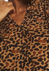 Camicia a fantasia leopardata marrone con scollatura a V, dettagli con bottoni e maniche corte, che mette in mostra una morbida texture del tessuto e un motivo vario.