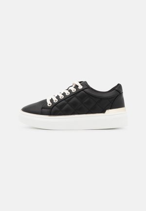 Black quilted sneaker with white laces and thick white sole, featuring a small silver detail near the heel on a plain light background.