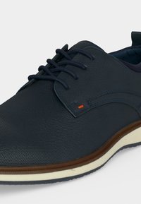 Chaussure en cuir texturé bleu foncé à lacets avec semelle en caoutchouc blanche et marron, avec un subtil détail de surpiqûre orange près des lacets.