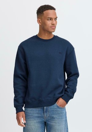 Donkerblauwe sweatshirt van zachte stof, met een ronde hals, geribbelde manchetten en een klein logo op de borst. Gepaard met lichte denim jeans.