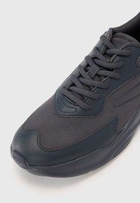 Navy athletic shoe featuring a textured fabric upper, reinforced toe, and laces. Smooth rubber sole with subtle branding detail near the heel.