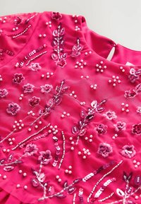 Roze stoffen top met bloemborduurwerk en pailletten. Heeft een textuursteek en kraalaccenten, met een ronde halslijn en een sleutelgaatje aan de achterkant.