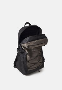 Sac à dos noir et gris avec poche zippée à l'avant, détail cordon élastique, poches latérales et fermeture éclair du compartiment principal partiellement ouverte.
