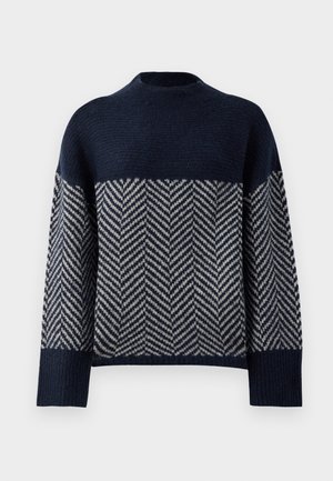 Mornarsko modra jopica z visokim ovratnikom, ki ima chevron vzorec v krem barvi. Teksturirana pletenina, padli ramena in rebrasti zaključki rokavov.
