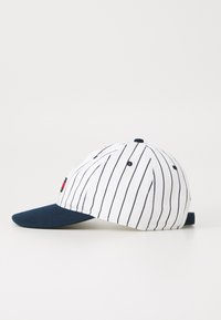 White cap with vertical navy stripes, navy brim, and an adjustable strap at the back. Features a small red logo on the front.
